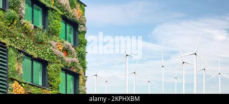 Extérieur d'un bâtiment vert durable recouvert de plantes suspendues verticales en fleurs devant des éoliennes Banque D'Images