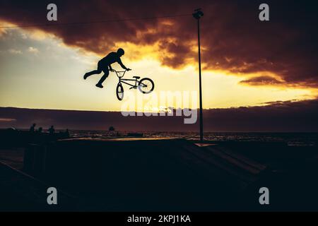 BMX rider faisant un whip de tailleur dans une rampe de skate Park avec un coucher de soleil dans le dos Banque D'Images