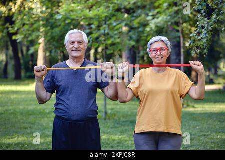 Senior 60 conjoints portent des vêtements de sport faire des exercices de mains, l'entraînement des armes à l'extérieur dans le parc d'été le matin à l'aide de bandes de caoutchouc de résistance. Li sain Banque D'Images