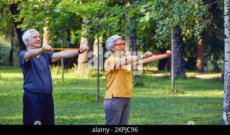 Senior 60 conjoints portent des vêtements de sport faire des exercices de mains, l'entraînement des armes à l'extérieur dans le parc d'été le matin à l'aide de bandes de caoutchouc de résistance. Li sain Banque D'Images