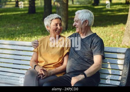 Joyeux couple de cheveux gris multiraciaux âgés de repos assis sur le banc dans le parc après une promenade, promenade matinale souriante Profitez de la détente à l'extérieur pendant l'été ensoleillé Banque D'Images