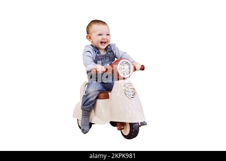 Un bébé joyeux, isolé sur fond blanc, fait une moto en plastique pour enfants dans la salle de jeux. Un enfant souriant conduit un jouet de mobylette, isolé sur un Banque D'Images