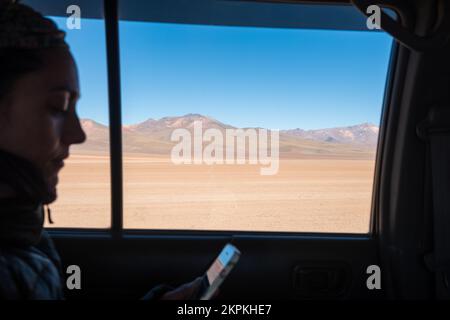 Femme à l'intérieur d'un véhicule qui vérifie son mobile en passant par l'Altiplano ou High Plains, département de Potosi, Bolivie Banque D'Images