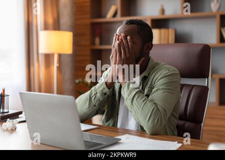 Un gars afro-américain d'âge moyen fatigué et triste couvre le visage avec des mains souffrant de surmenage Banque D'Images