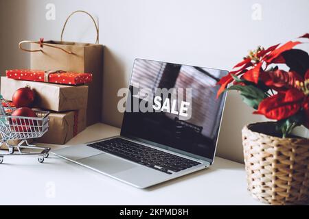 Ordinateur portable ouvert avec Word sale sur écran d'affichage, Poinsettias fleur de Noël et boîtes-cadeaux sur table blanche. Achats en ligne de Noël, hiver Banque D'Images