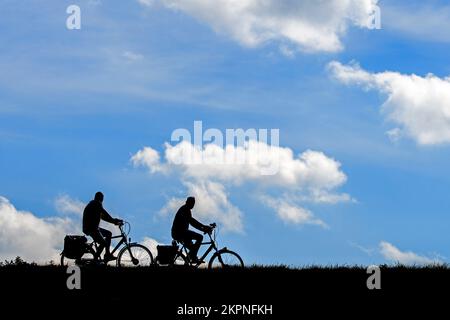 En été, deux cyclistes âgés ont silhoueté à vélo contre le ciel nuageux Banque D'Images