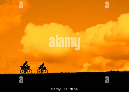 Couple de jeunes cyclistes qui ont fait leurs tournées en vélo silhoueté contre le ciel orangé de coucher de soleil en été Banque D'Images