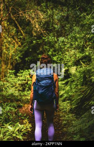 Description: Femme athlétique avec sac à dos marche à travers la jungle aventureuse chemin le long de vert surgrown chemin. Levada de Caldeirão Verde, île de Madère, Banque D'Images