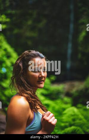 Description: Femme sportive se présente dans la nature à une impressionnante cascade dans la jungle avec de belles fleurs et fougères. Levada de Caldeirão Verde, fabriqué Banque D'Images