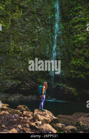 Description: Belle femme athlétique avec sac à dos regardant la cascade de haute jungle étonnante. Levada de Caldeirão Verde, île de Madère, Portugal, EUR Banque D'Images