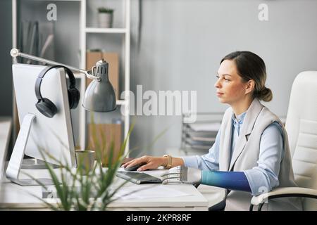 Jeune femme d'affaires avec un bras prothétique travaillant sur un ordinateur au bureau Banque D'Images