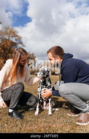 Le couple joue avec son chien dalmate sur la marche dans le parc Banque D'Images