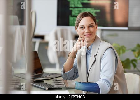 Portrait d'une chercheuse souriante avec un bras prothétique assis à son bureau Banque D'Images