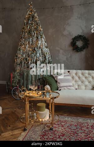 Vélo enveloppé d'un arc à côté d'un sapin de Noël dans un salon avec un canapé et une table latérale décorée de lumières de Noël Banque D'Images