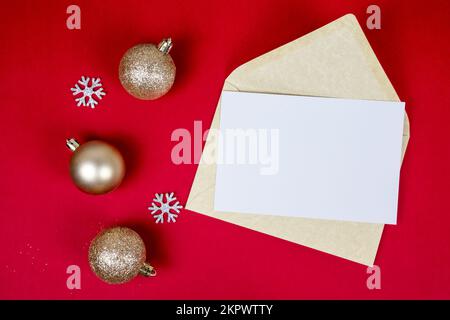 Maquette de la lettre de Noël avec enveloppe et décoration de boules de noël dorées sur fond rouge avec espace de copie et flocons de neige, vue du dessus. Banque D'Images