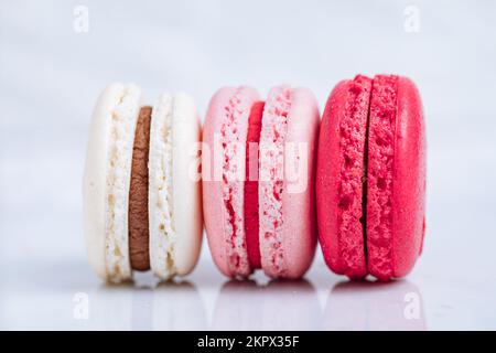 Gros plan de macarons de différentes couleurs sur fond blanc lumineux avec reflets subtils sur le plateau en marbre Dessert populaire de merengue avec des boîtes de remplissage Banque D'Images