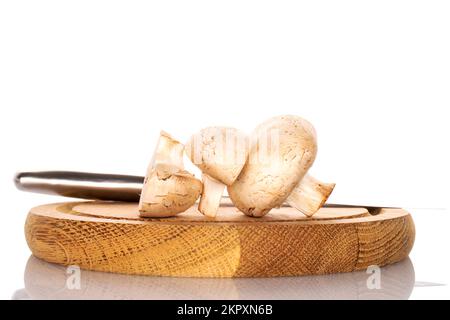 Une moitié entière et deux moitiés de champignons frais bio champignon sur un plateau rond en bambou avec un couteau en métal, gros plan, sur fond blanc. Banque D'Images