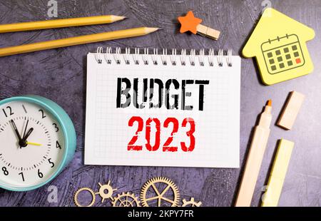 Bloc-notes avec texte BUDGET 2023, lunettes, trombones, calculatrice blanche et stylo sur le bureau, vue de dessus Banque D'Images