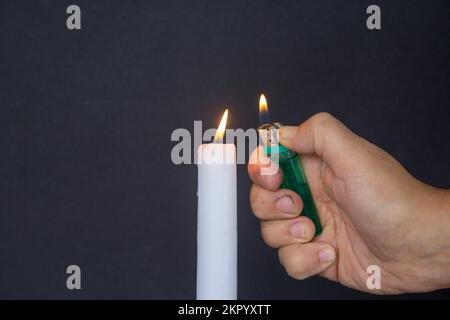 Main d'un homme tenant un briquet tout en éclairant une bougie sur un fond noir. Banque D'Images