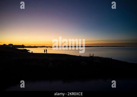 Les gens qui marchent sur la plage au coucher du soleil Banque D'Images