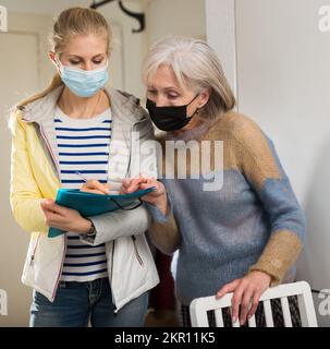 La femme mûre dans le masque de protection répond aux questions de l'intervieweur à la maison Banque D'Images