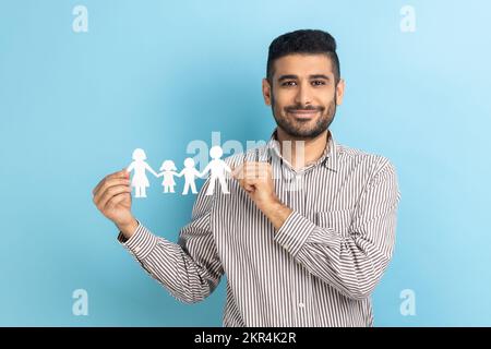 Portrait d'un homme d'affaires barbu tenant la chaîne de papier entre les mains, concept de famille heureuse, parent, enfance, portant une chemise rayée. Studio d'intérieur isolé sur fond bleu. Banque D'Images