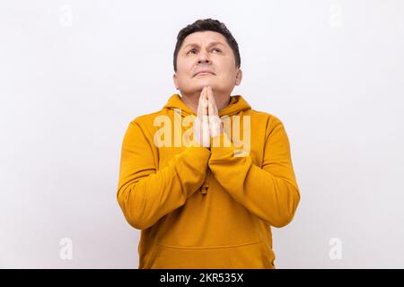 Portrait d'un beau homme d'âge moyen priant avec cœur, se sentant coupable, pleurant l'aide du ciel, portant un sweat à capuche de style urbain. Studio d'intérieur isolé sur fond blanc. Banque D'Images