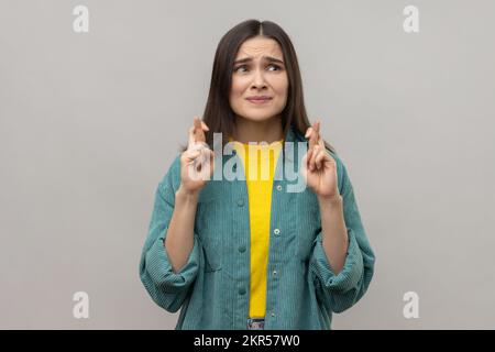 Portrait de la femme debout avec les doigts croisés pour la bonne chance, faisant le souhait de coeur, priant et espérant pour le miracle, portant une veste de style décontracté. Prise de vue en studio isolée sur fond gris. Banque D'Images