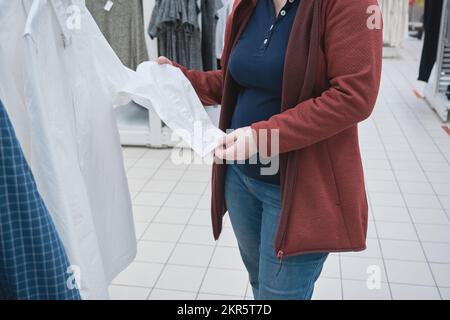 Une femme enceinte du magasin choisit une nouvelle chemise blanche pour son mari Banque D'Images
