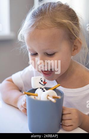 Les petits enfants mignons mangent un bonhomme de neige marmmello décoré de glace et de boissons de cacao. Banque D'Images
