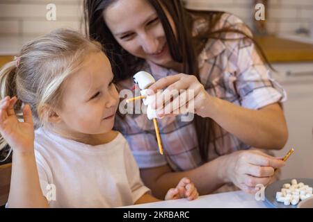 Les parents et les enfants font des bonshommes de neige à partir de guimauves. Ils boivent du cacao et se préparent pour Noël. Concept de la maison de Noël. Banque D'Images