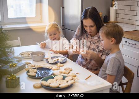 Les parents et les enfants font des bonshommes de neige à partir de guimauves. Ils boivent du cacao et se préparent pour Noël. Concept de la maison de Noël. Banque D'Images