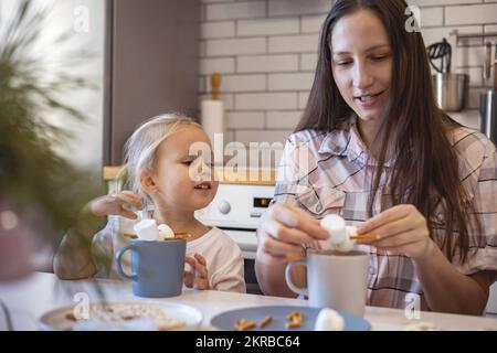 Les parents et les enfants font des bonshommes de neige à partir de guimauves. Ils boivent du cacao et se préparent pour Noël. Concept de la maison de Noël. Banque D'Images