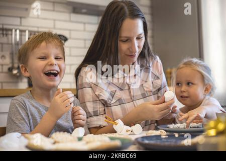 Les parents et les enfants font des bonshommes de neige à partir de guimauves. Ils boivent du cacao et se préparent pour Noël. Concept de la maison de Noël. Banque D'Images