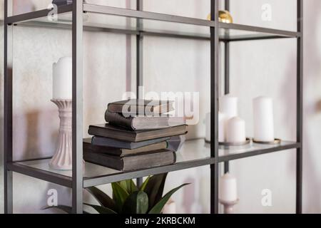 étagère en métal avec différents livres, bougies blanches et plante sur fond de mur blanc Banque D'Images