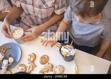 Les parents et les enfants font des bonshommes de neige à partir de guimauves. Ils boivent du cacao et se préparent pour Noël. Concept de la maison de Noël. Banque D'Images