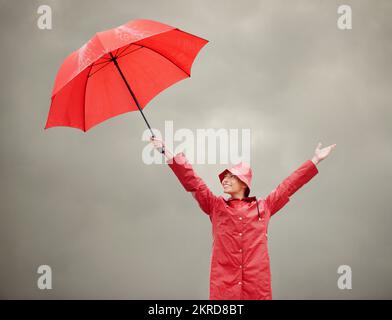 Maintien de la positivité. Une belle jeune femme debout dehors tout en tenant son parapluie rouge. Banque D'Images