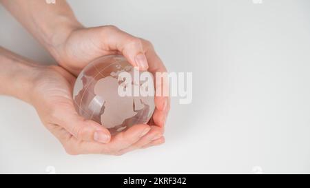 Globe en cristal dans les mains des femmes sur fond blanc. Banque D'Images