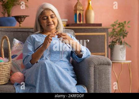 Une vieille femme triant tout en étant assise sur un canapé dans la salle de séjour Banque D'Images