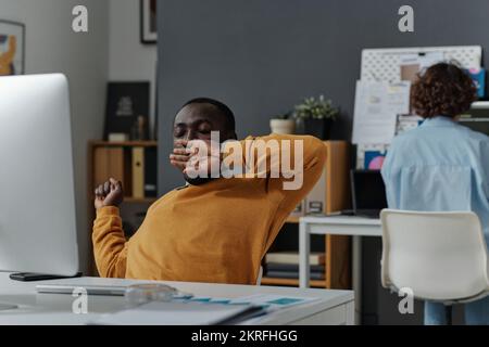 Un jeune programmeur afro-américain fatigué de son travail à l'ordinateur, il s'est assis sur son lieu de travail et bâillant Banque D'Images