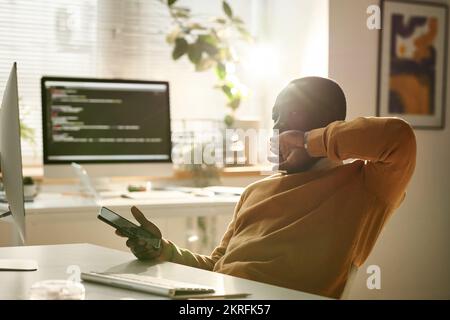 Un développeur informatique afro-américain lasse l'utilisation d'un smartphone au travail lorsqu'il travaille au bureau Banque D'Images