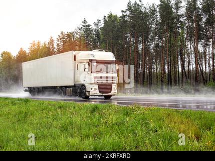 un camion blanc moderne avec semi-remorque transporte des cargaisons par temps pluvieux sur fond de forêt Banque D'Images