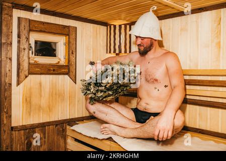 Homme avec un balai relaxant dans le sauna Banque D'Images