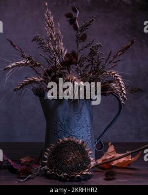 Les fleurs et les plantes séchées sont récoltées dans un vase en étain vintage et sur une table en bois Banque D'Images