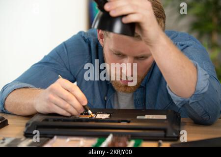 jeune homme beau répare un ordinateur portable Banque D'Images