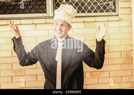 Portrait amusant d'un cuisinier mâle agitant les mains dans l'air avec des bouffées de farine volante. Jeter rapidement ensemble Banque D'Images