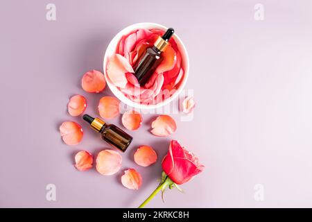 Vue de dessus des flacons cosmétiques en verre foncé avec une pipette avec un produit naturel biologique pour le soin du visage. arrière-plan pastel. pétales de rose. Banque D'Images