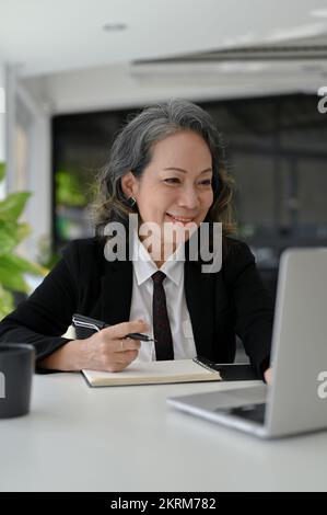 Portrait, femme d'affaires asiatique charmante et réussie en costume d'affaires formel travaillant à son bureau, à l'aide d'un ordinateur portable. Banque D'Images