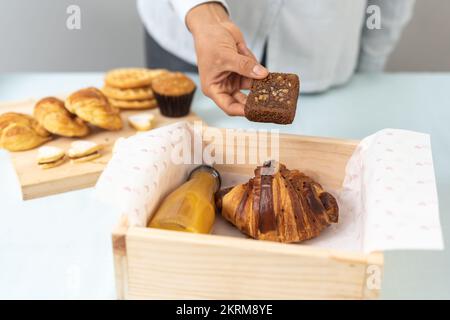 Du dessus de la récolte confiserie anonyme en mettant un morceau de pain de banane fraîchement cuit dans une boîte avec croissant croquant et une bouteille de jus d'orange en ca Banque D'Images