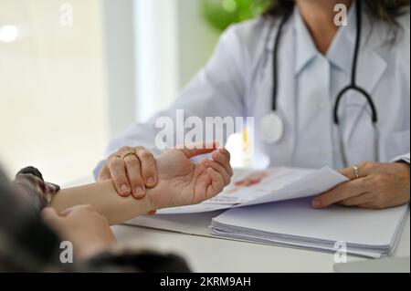 Prise de vue rapprochée et rognée, médecin asiatique professionnel de sexe féminin vérifiant le pouls du patient sur sa main. Banque D'Images